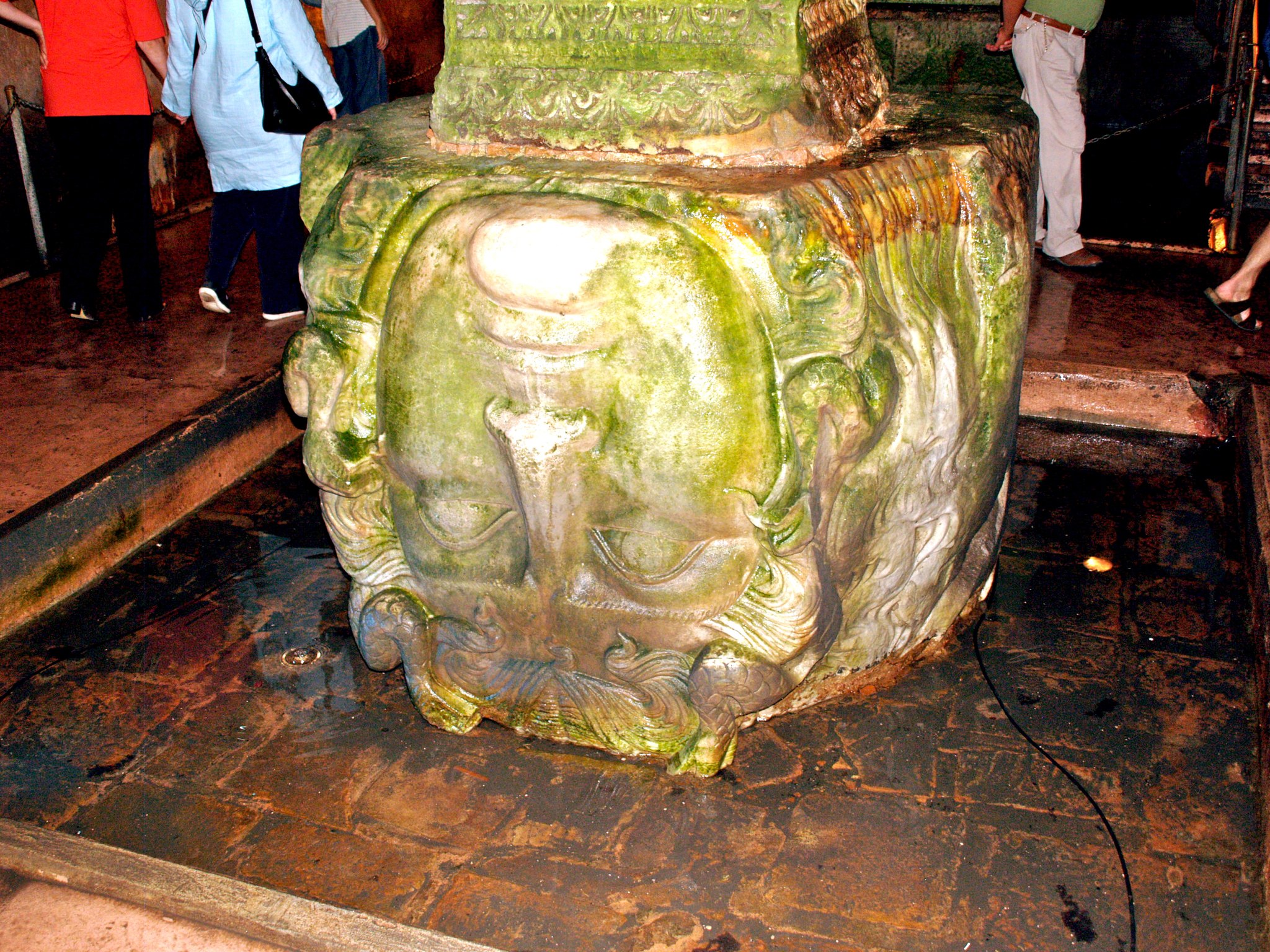 One of the Medusa head column bases in the Basilica Cistern, with visitors standing beside it for scale
