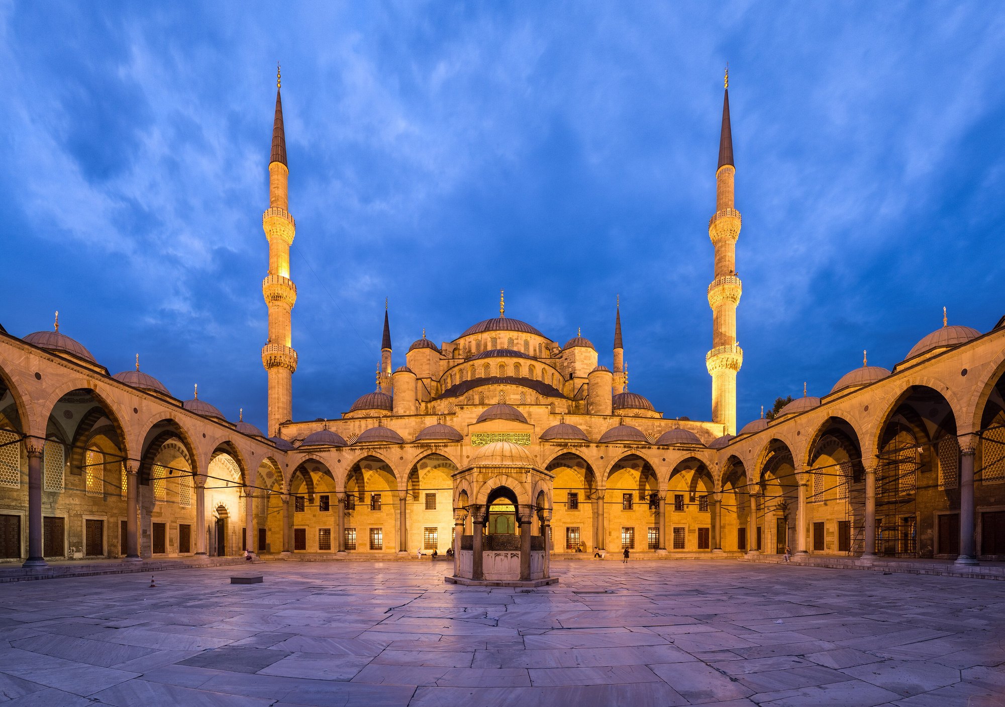 The courtyard of the Blue Mosque at dusk, the arcade lit from within and the domes stacked above it