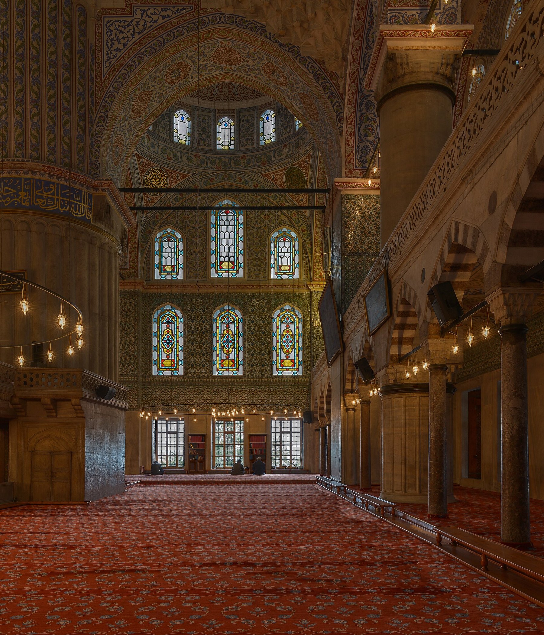 Inside the Blue Mosque, the painted arches and stained glass of the prayer hall in dim light