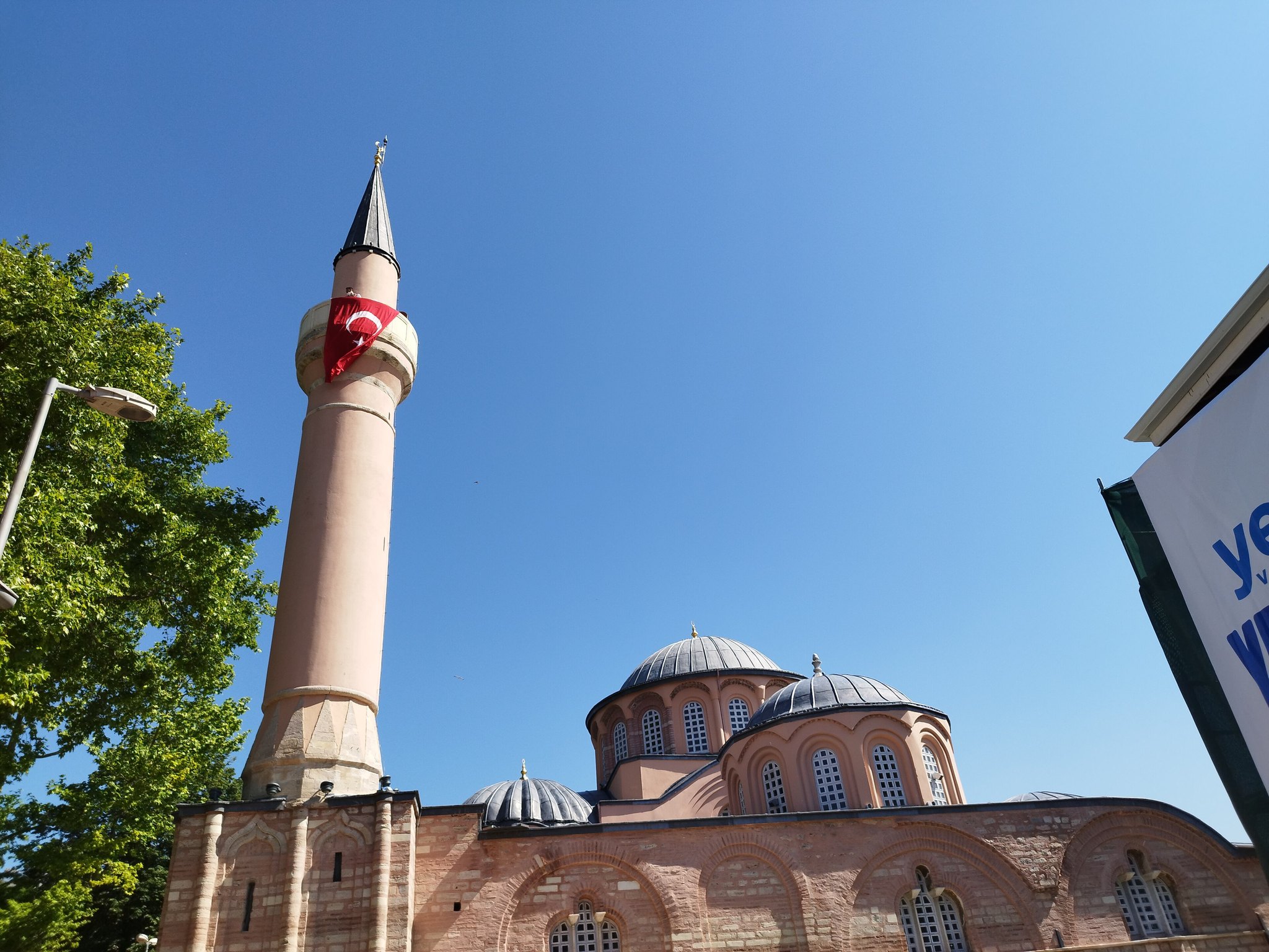 The exterior of the Chora church, its brick domes and single minaret against a blue sky