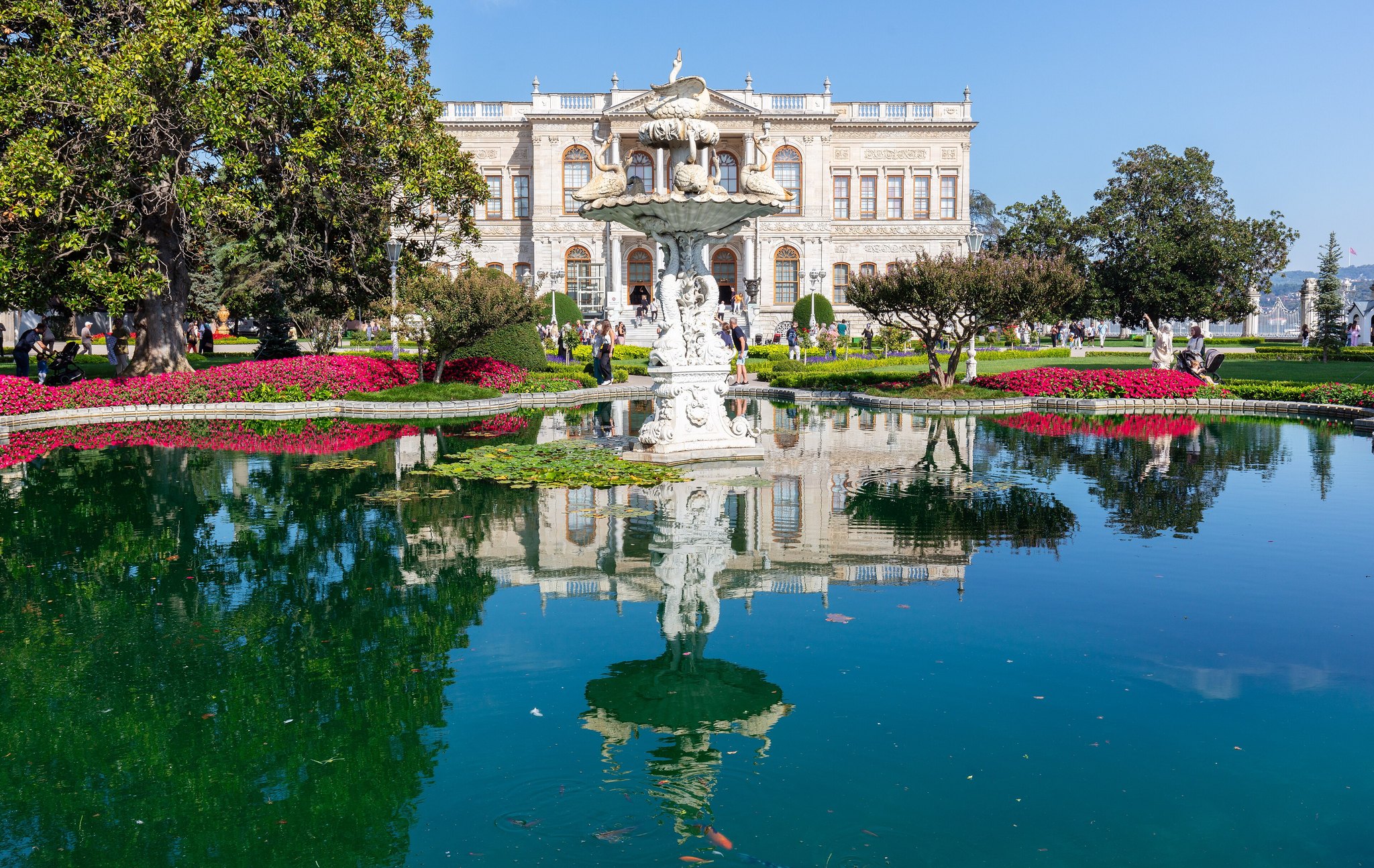 Dolmabahce Palace reflected in the pool of its garden, with flower beds in the foreground