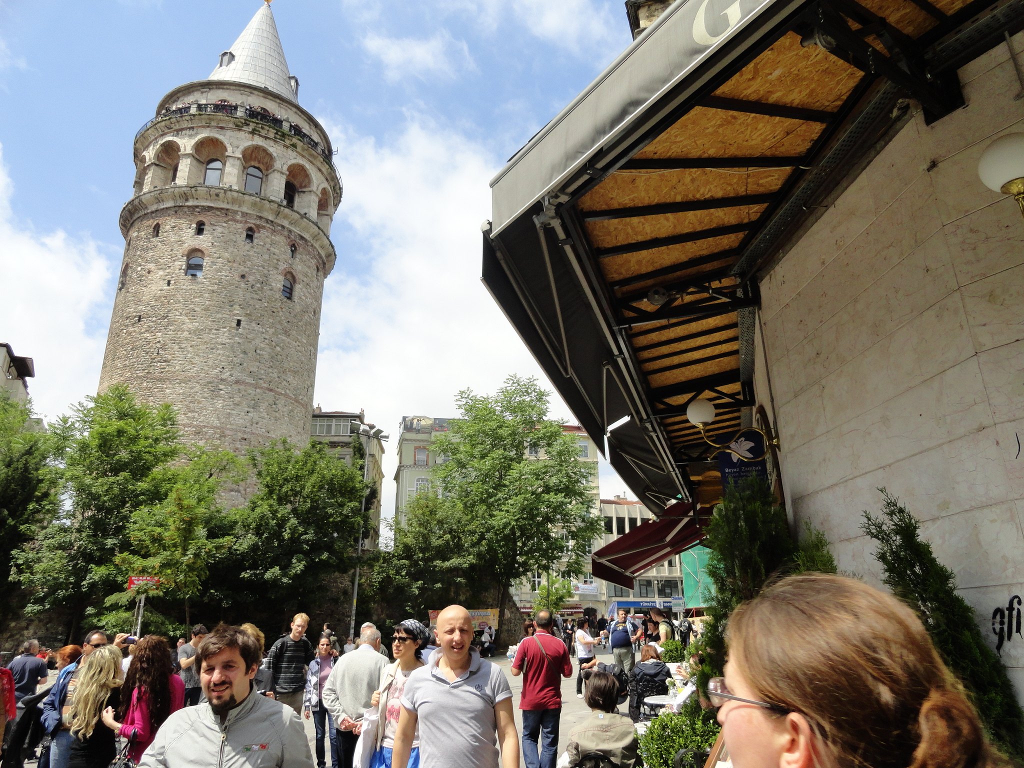 The base of the Galata Tower with the queue and the cafe awnings around the little square