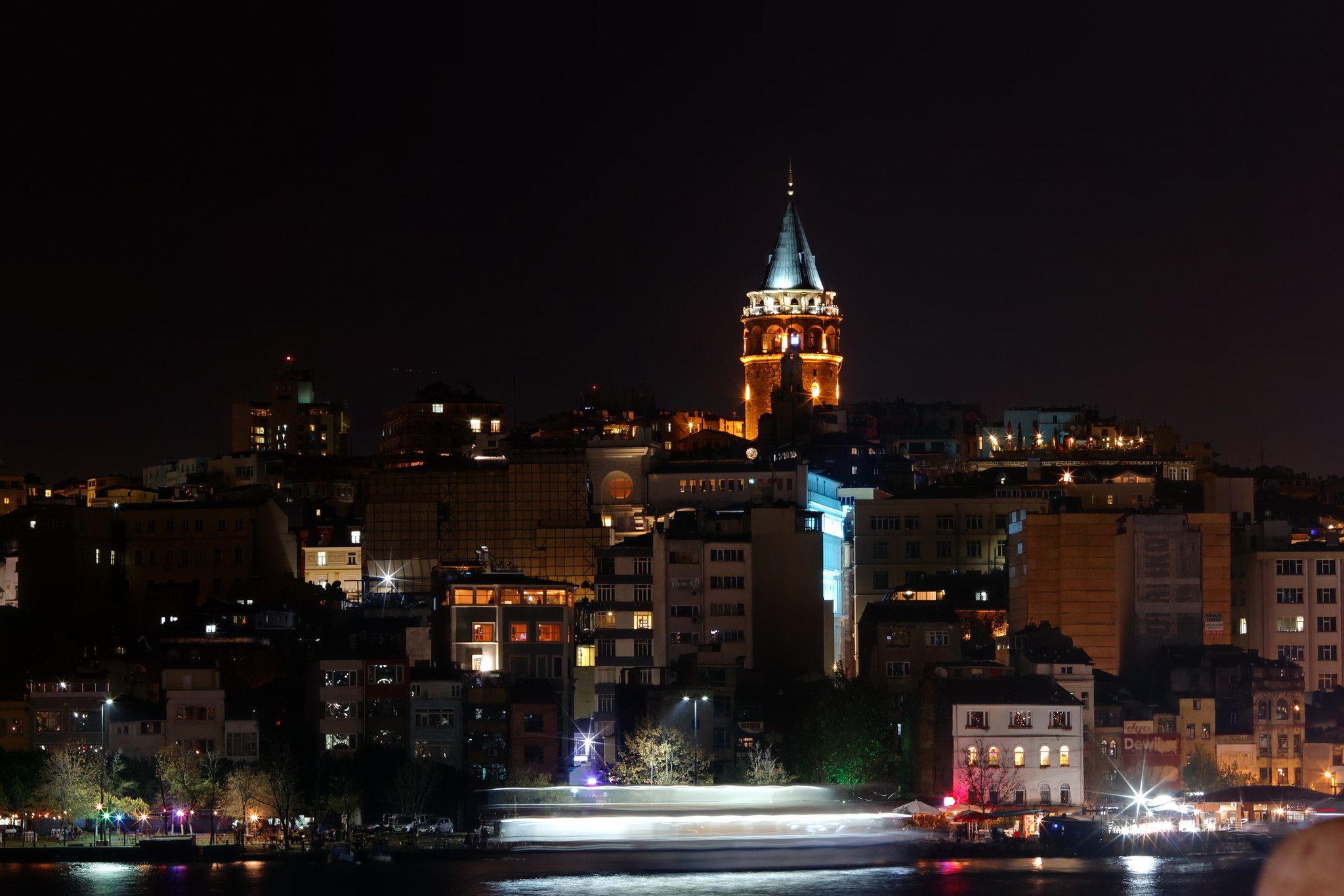 The Galata Tower lit at night above the dark city, seen across the water
