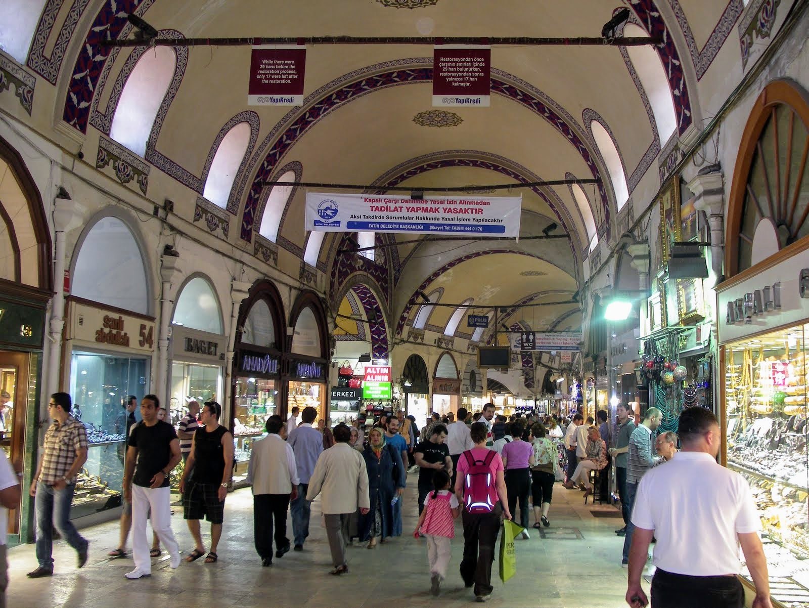 A vaulted lane of the Grand Bazaar crowded with shoppers, shopfronts on both sides under the painted arches