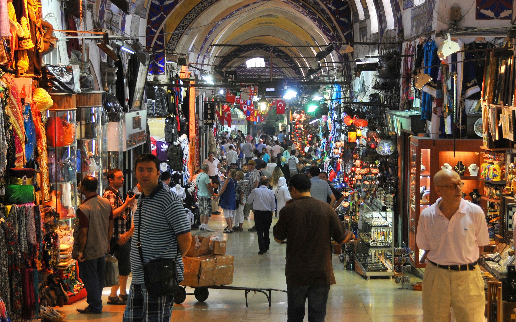 A Grand Bazaar lane hung with lamps and bags, a porter pushing a trolley through the crowd