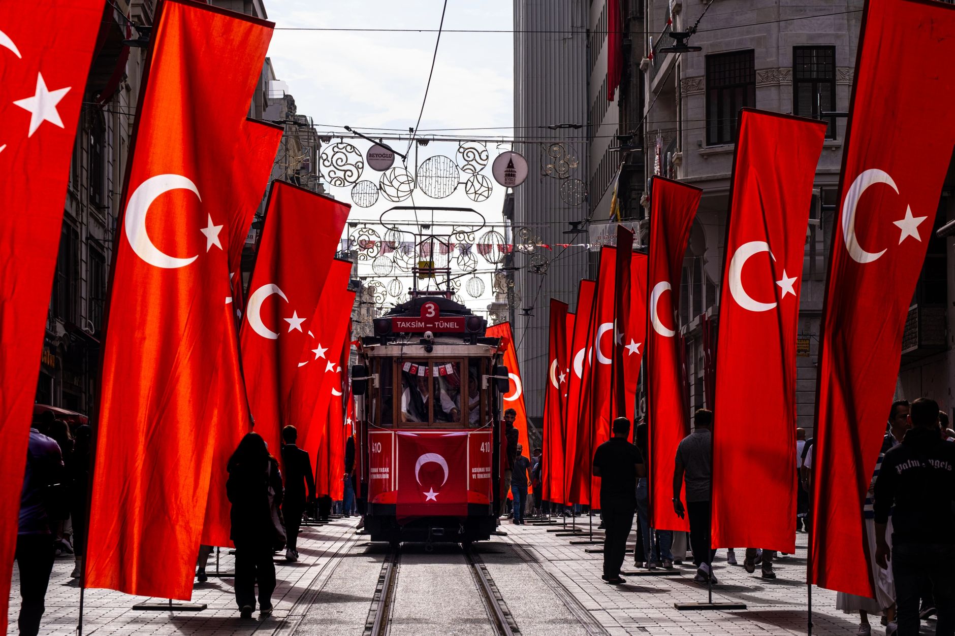 A classic red tram surrounded by Turkish flags in Istanbul, Türkiye, on a city street