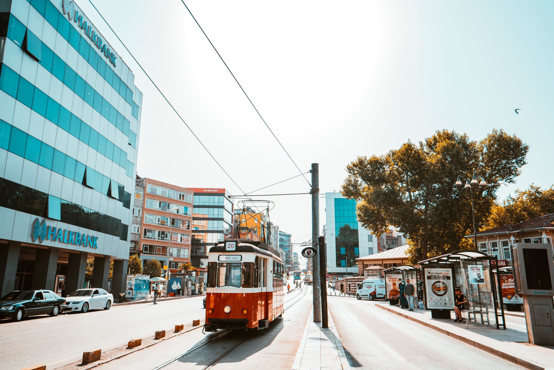 A classic red tram gliding through a sunlit street in Istanbul, flanked by modern buildings and lush trees