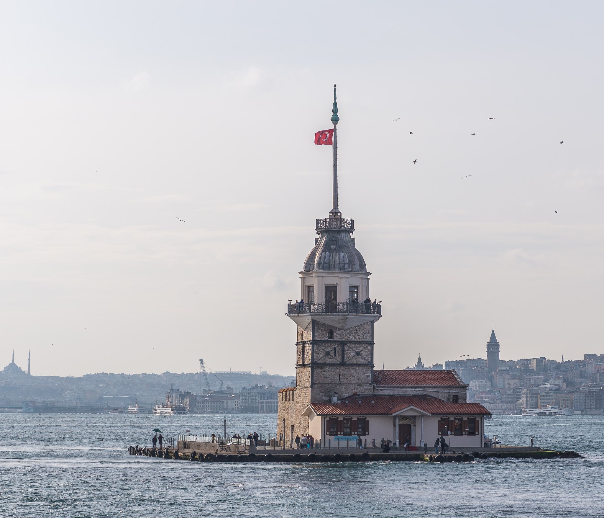 The Maiden's Tower alone in the strait under a clear sky, a flag at its mast