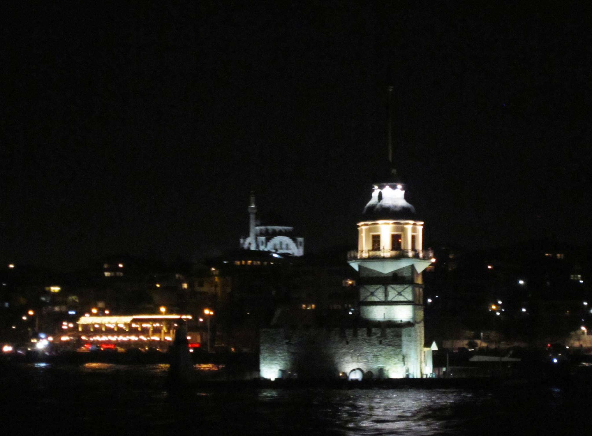 The Maiden's Tower lit at night, its reflection breaking on the dark water