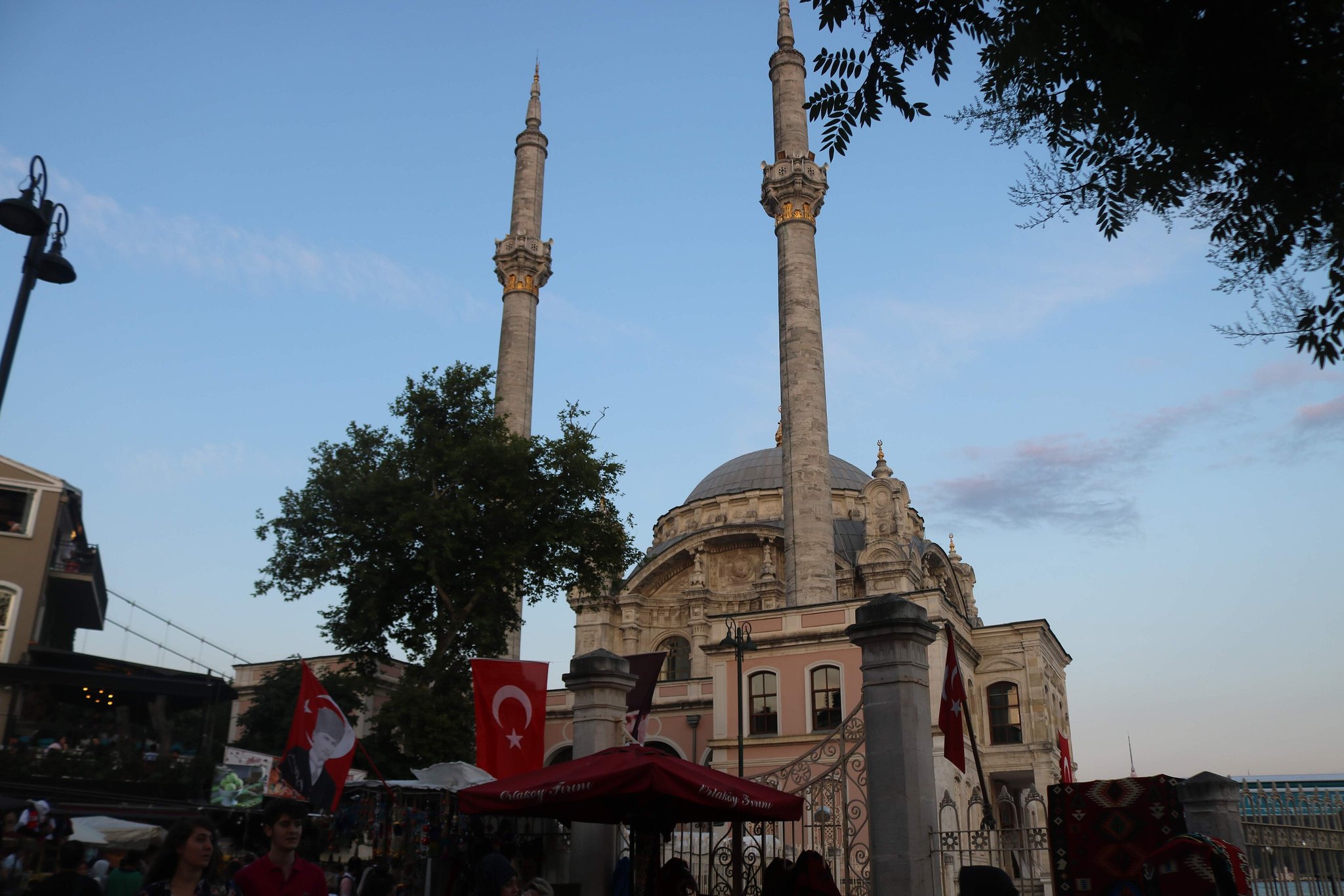 The square beside Ortakoy Mosque at street level, cafe umbrellas and a Turkish flag