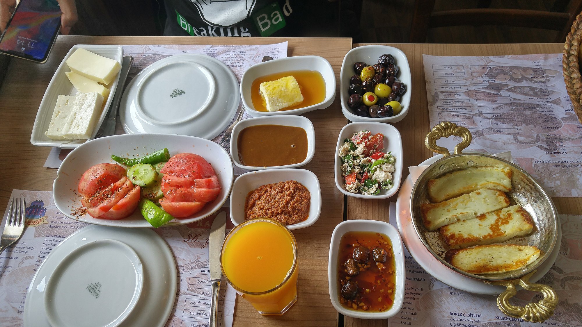 A full Turkish breakfast laid out: cheese, olives, tomato, jam, eggs and bread with tea and juice