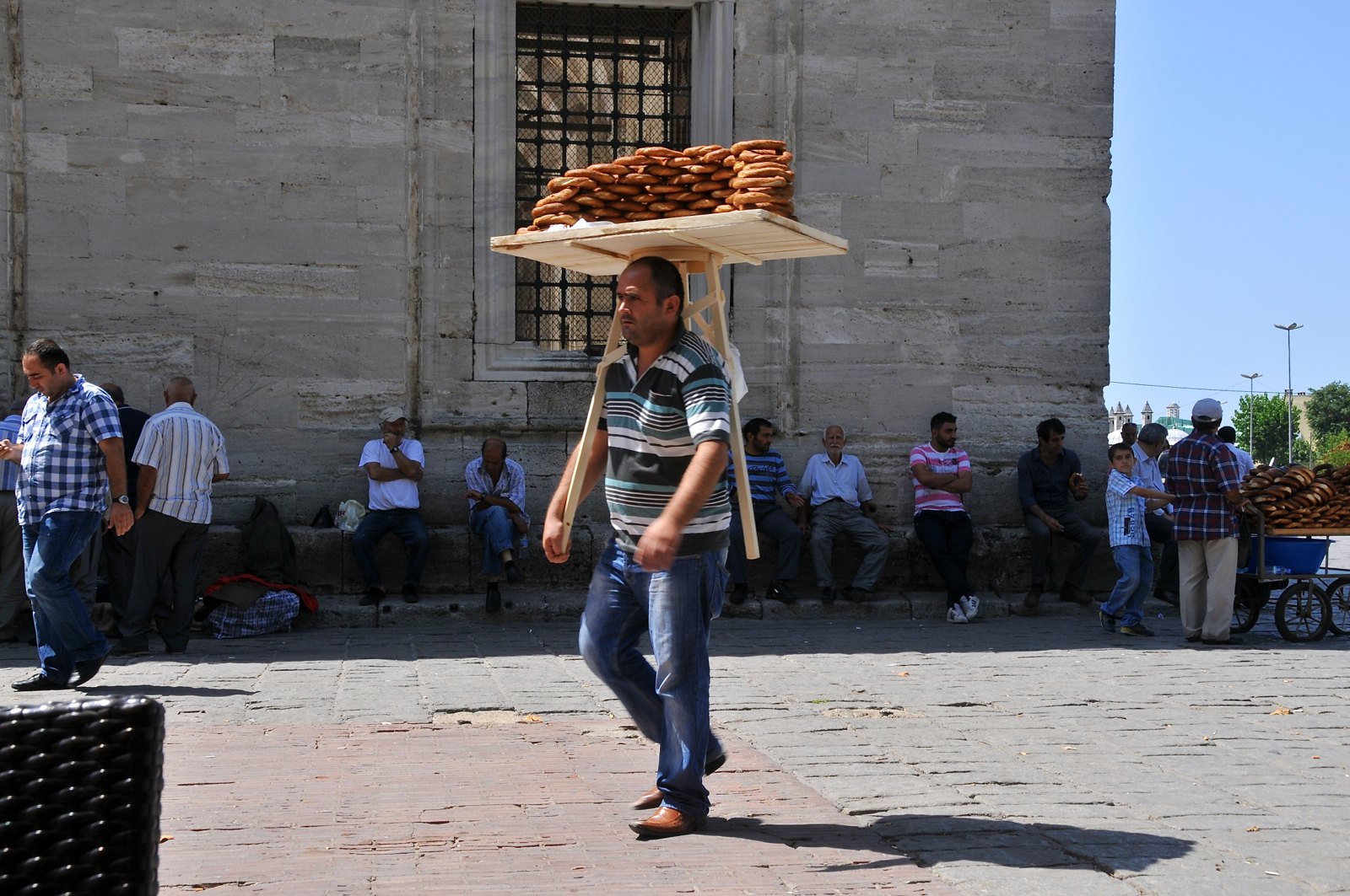 A simit seller crossing a square in Istanbul with a tray of sesame rings balanced on his head