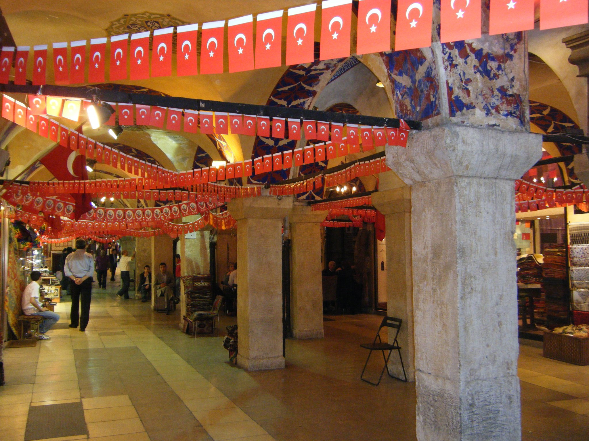 A Grand Bazaar arcade strung with red flags, shopfronts running away beneath the painted vault