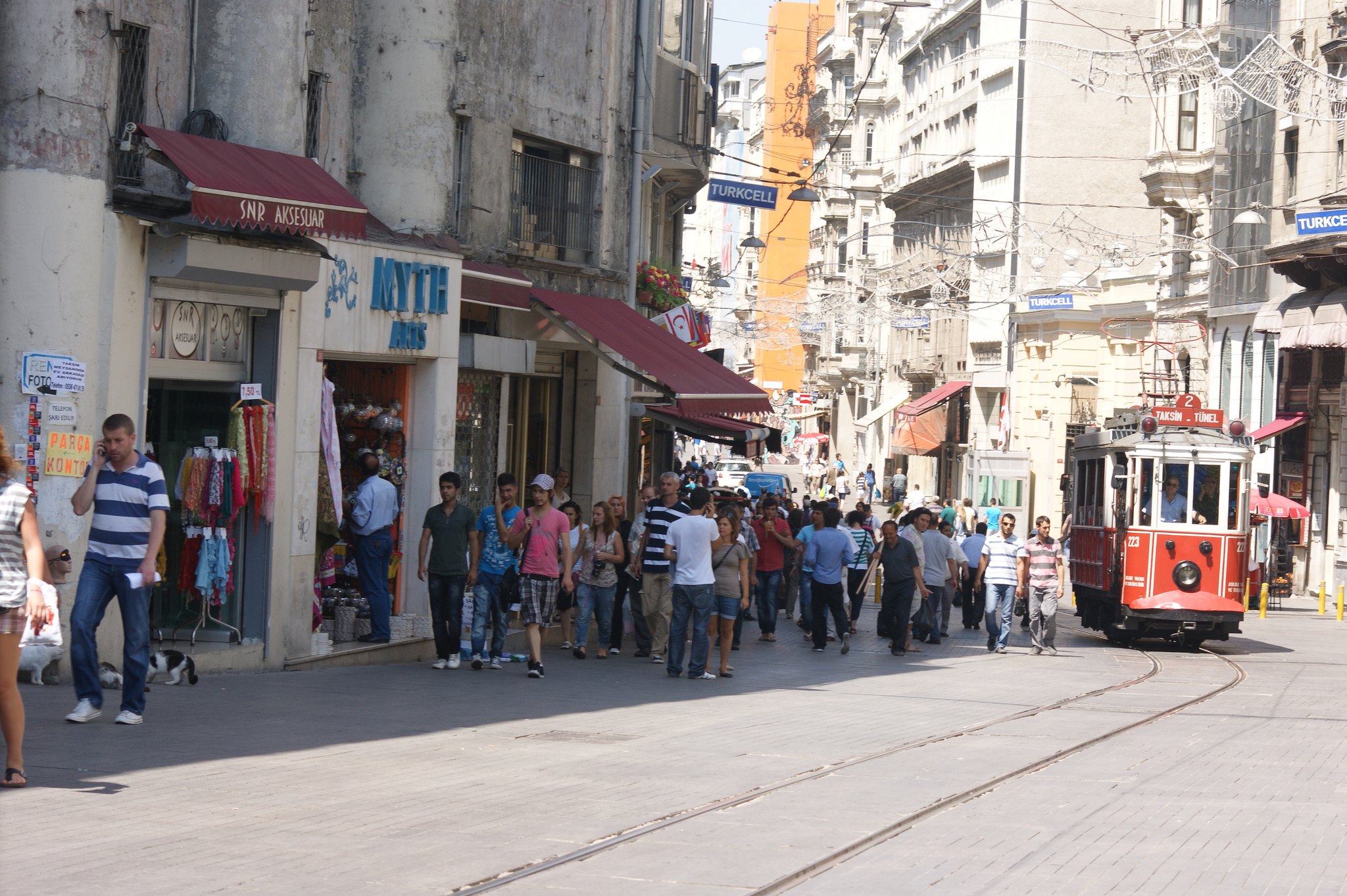 A busy Istanbul shopping street with tram rails down the middle and people crossing between them