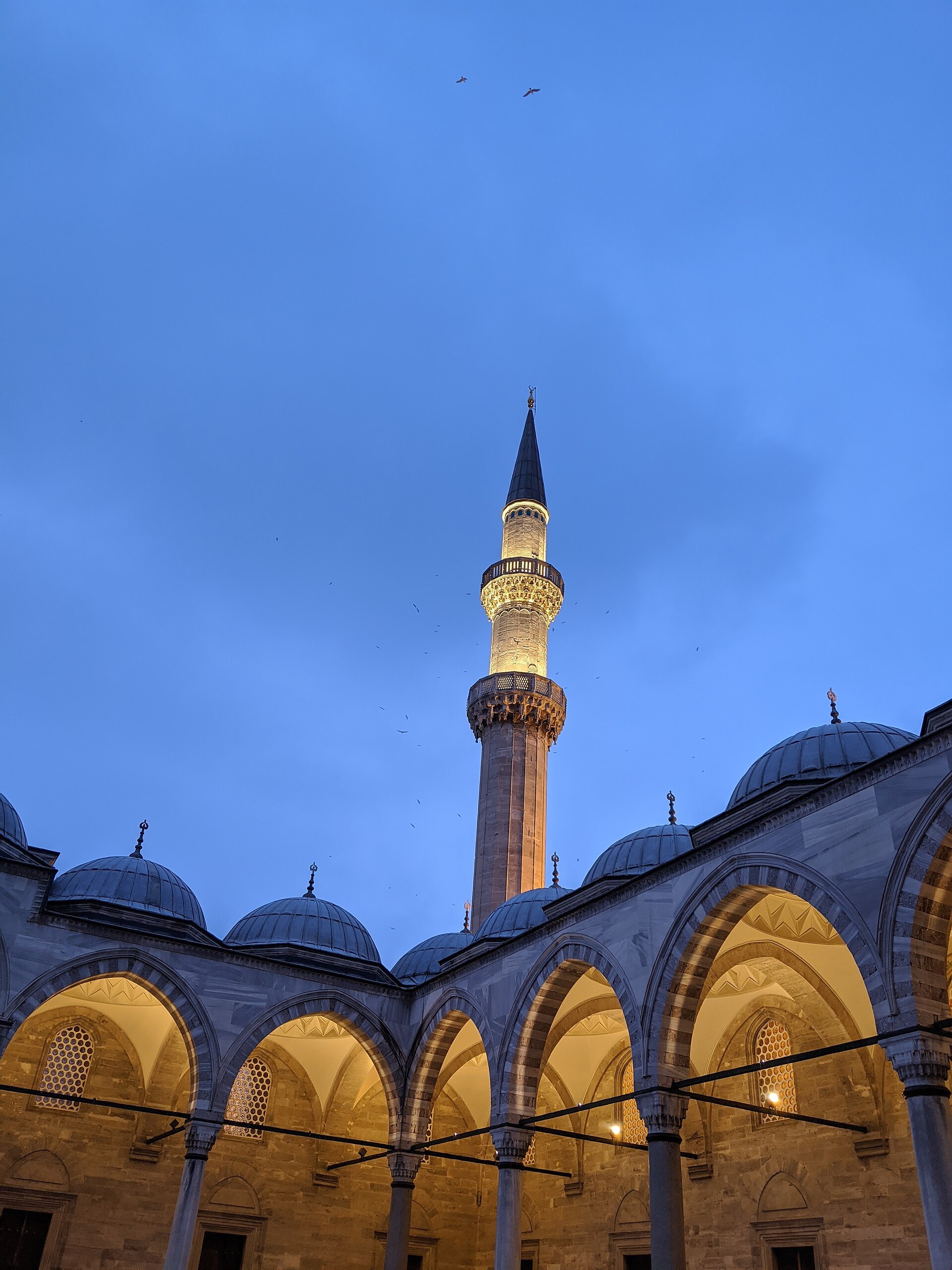 A minaret of the Suleymaniye Mosque lit gold against the blue of the sky just after sunset