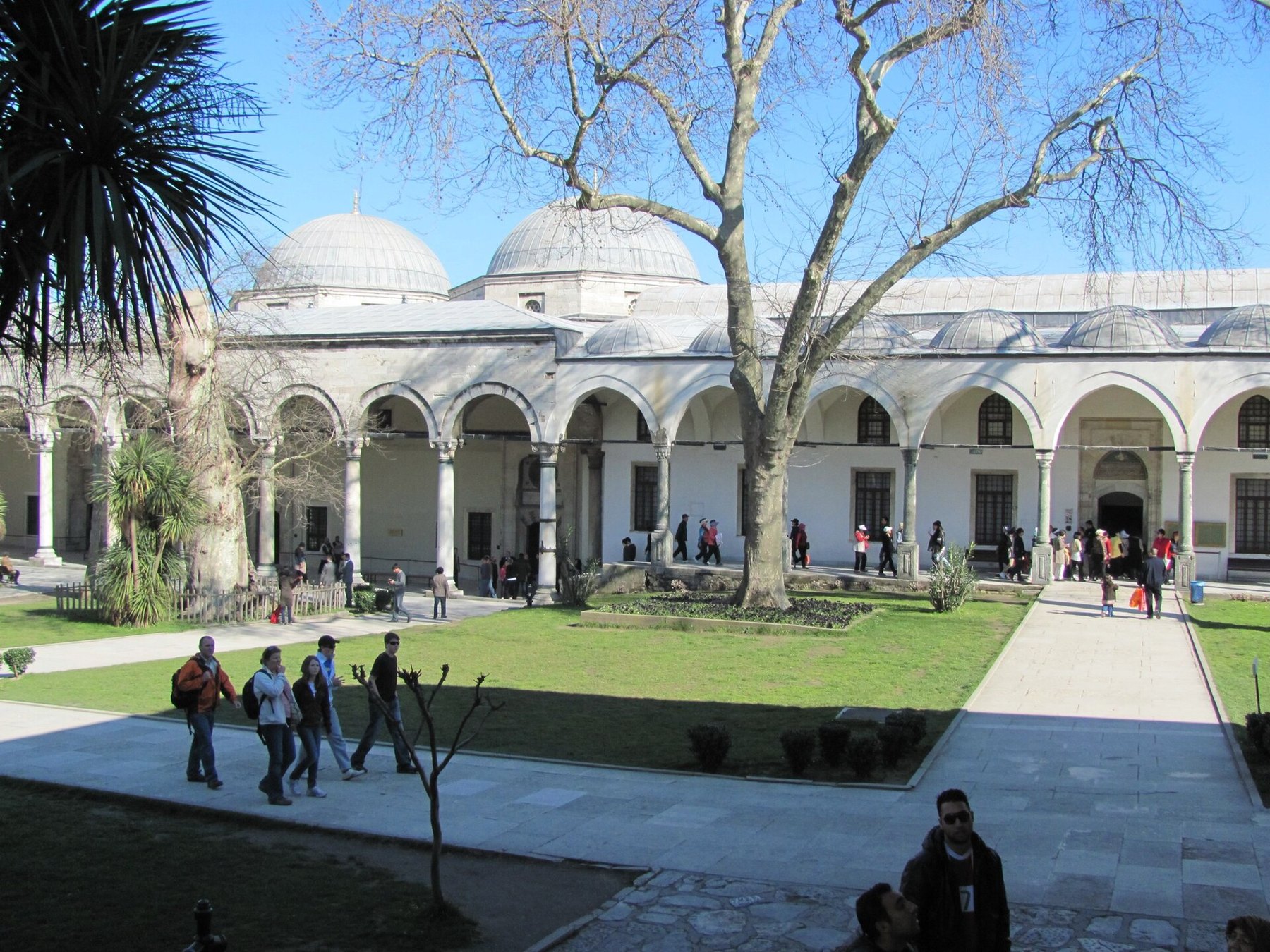 The colonnaded courtyard of Topkapi Palace, white marble arcade around a lawn with visitors crossing it