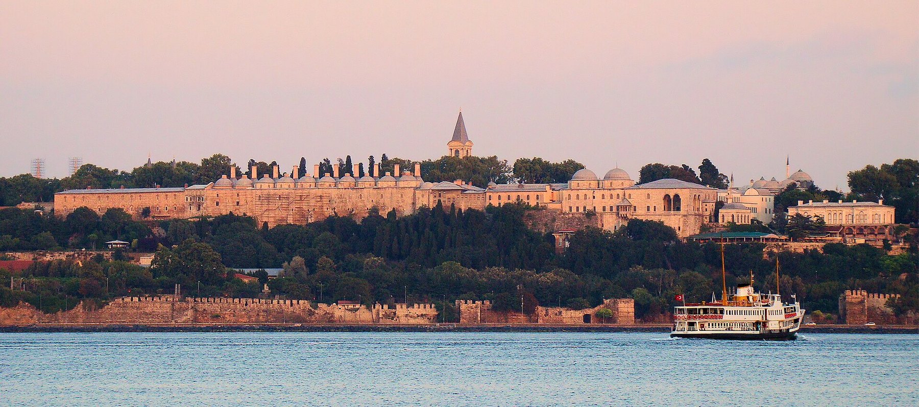 Topkapi Palace seen from the water at sunset, its walls and pavilions along the ridge above the Bosphorus